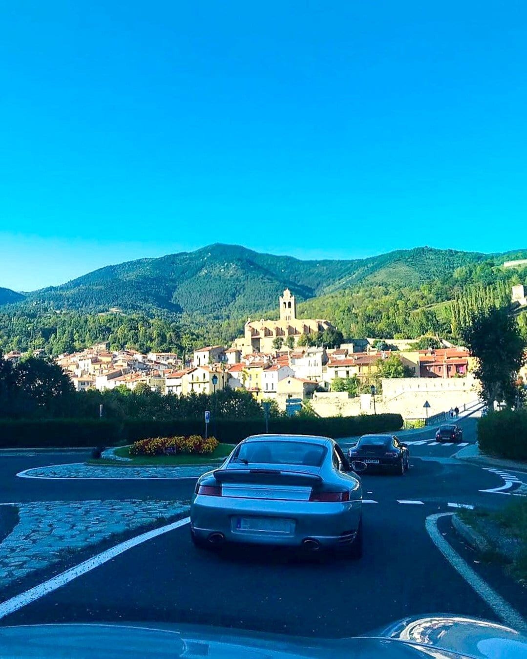 Un 996 Turbo blau en una rotonda, amb un poble de muntanya al fons, al II Endurance