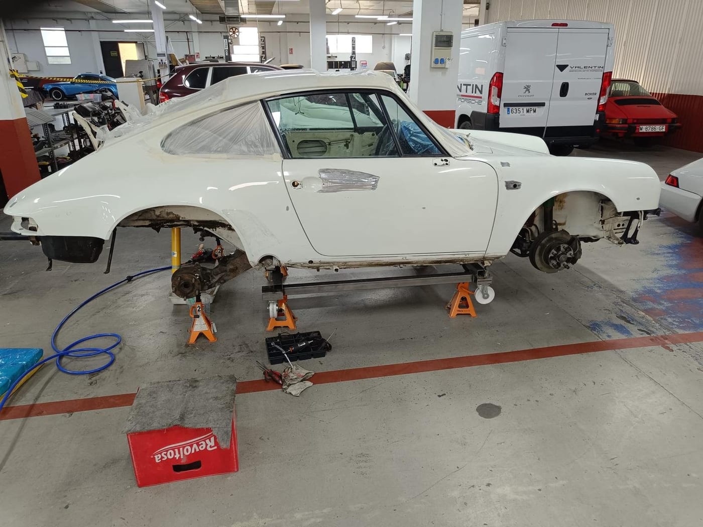 The white G-series 911 on axle stands, wheels off and mid-preparation