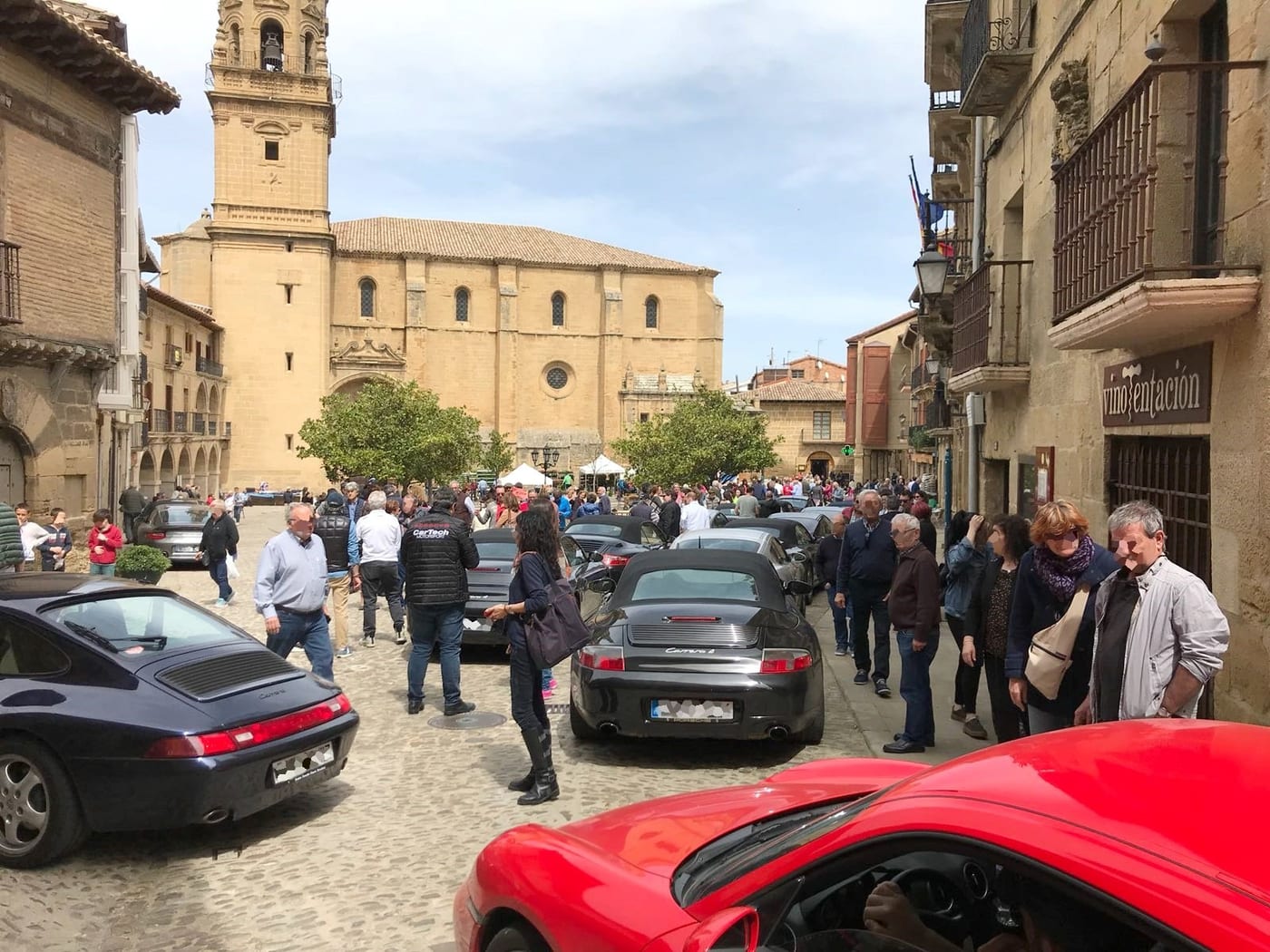 Els Porsche de l'esdeveniment de la Rioja Alta aparcats en un carrer amb l'església al fons