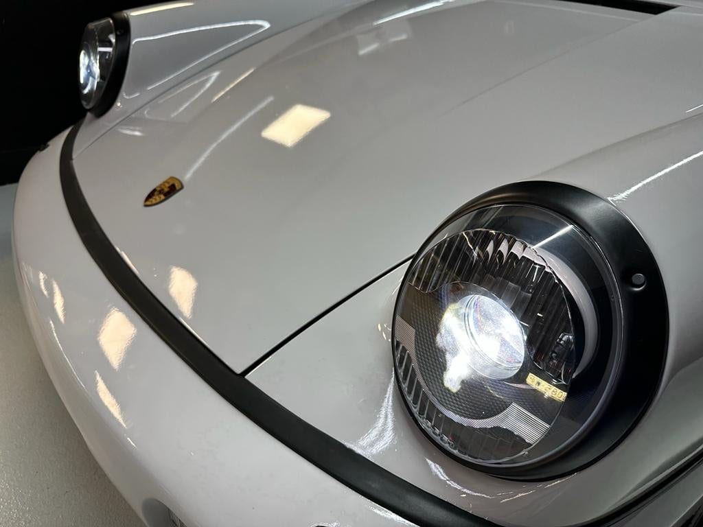 Frontal del 964 blanco con el faro LED encendido y el escudo Porsche sobre el capó