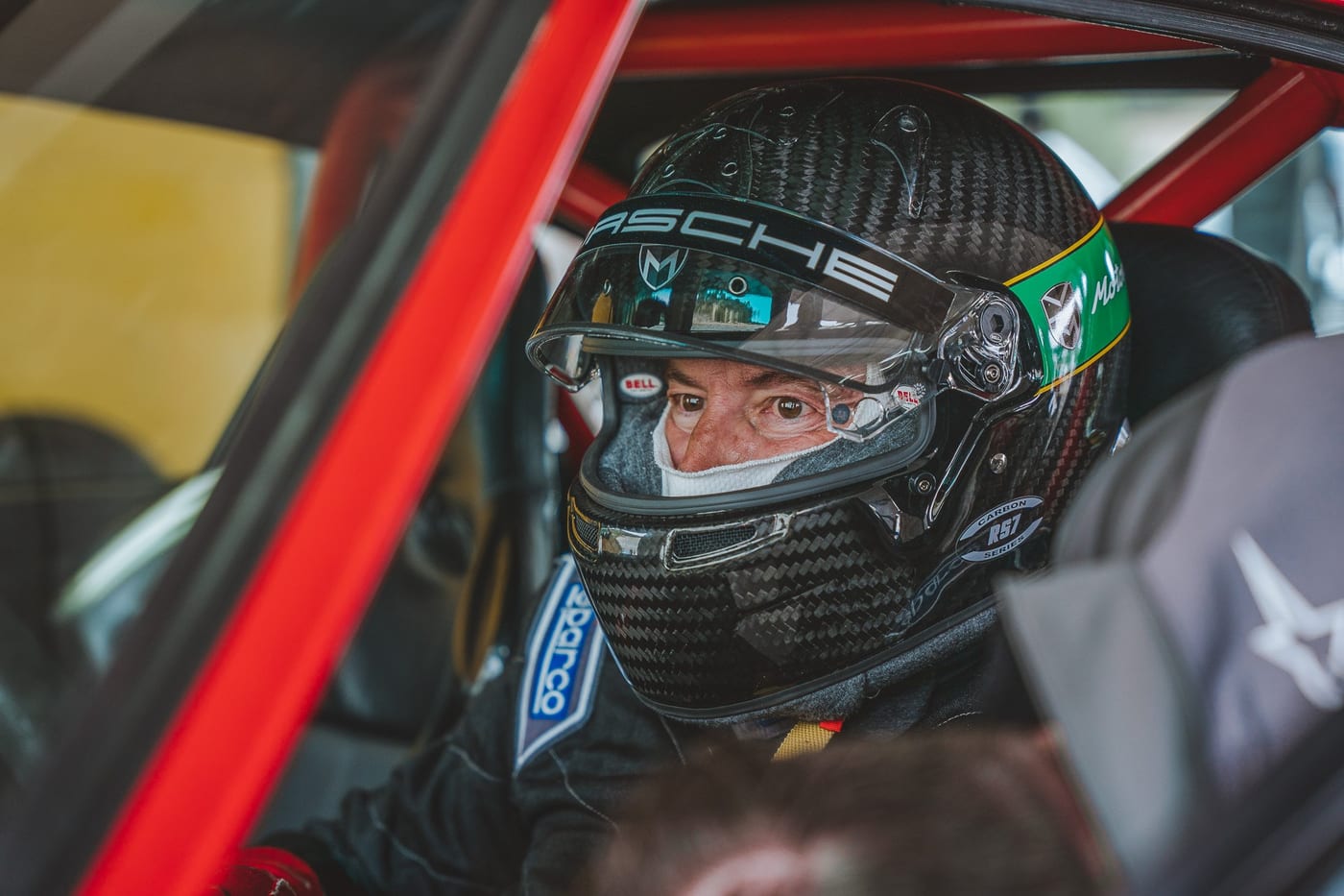 El piloto con el casco puesto dentro del 964 rojo, con la jaula amarilla detrás