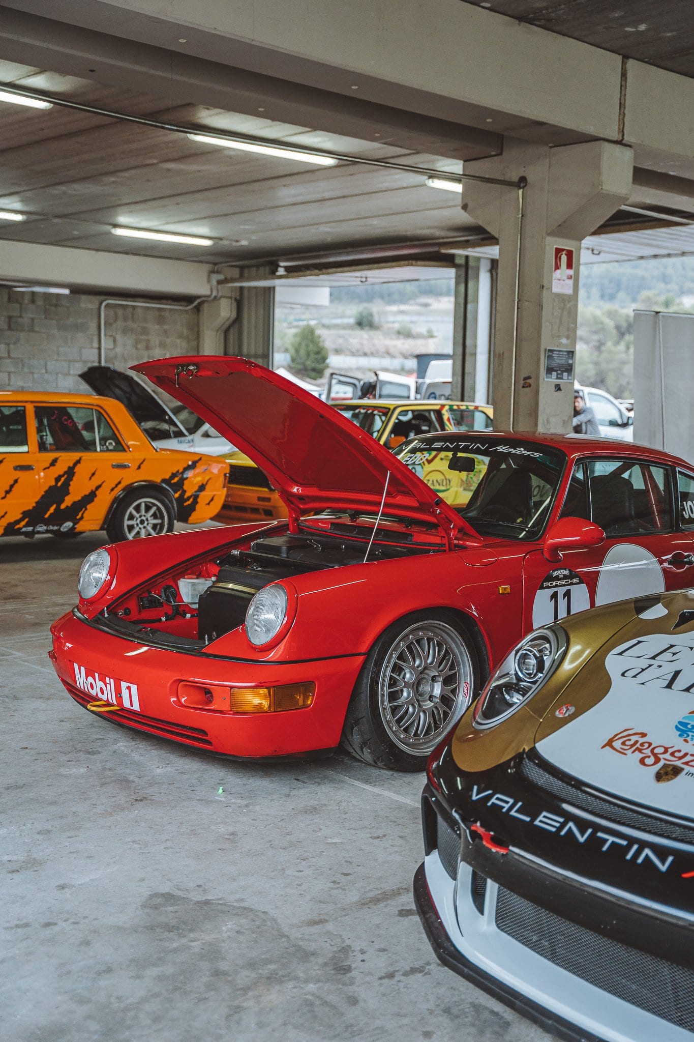 El 964 RS rojo con el capó abierto en el box, junto a otros coches del equipo