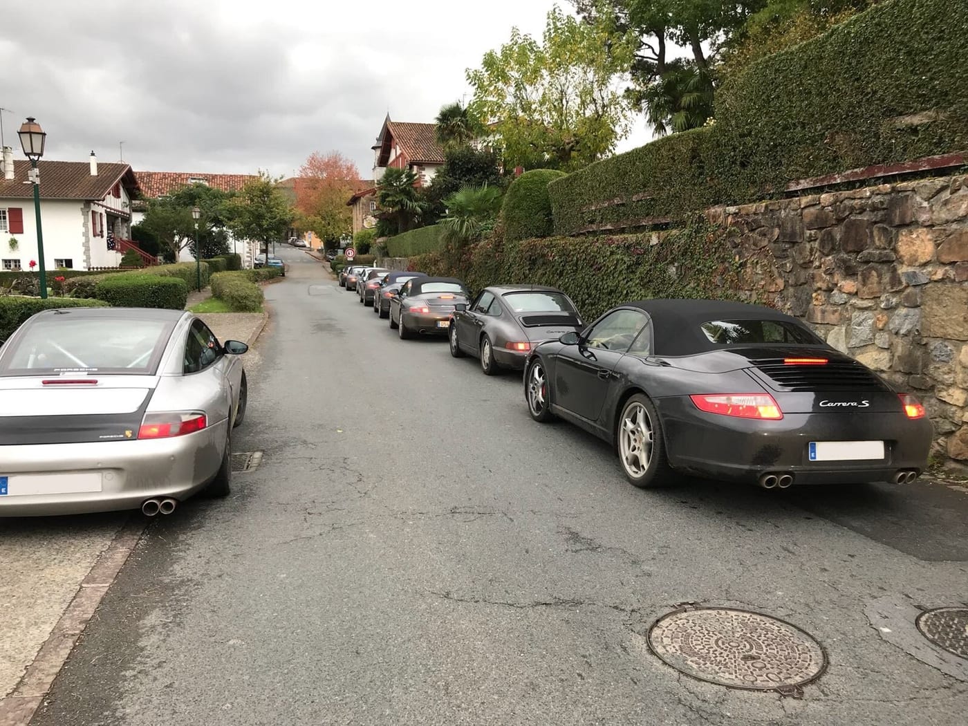 Els Porsche del Winter Ride 2017 aparcats en un carrer de poble, en filera al costat del mur