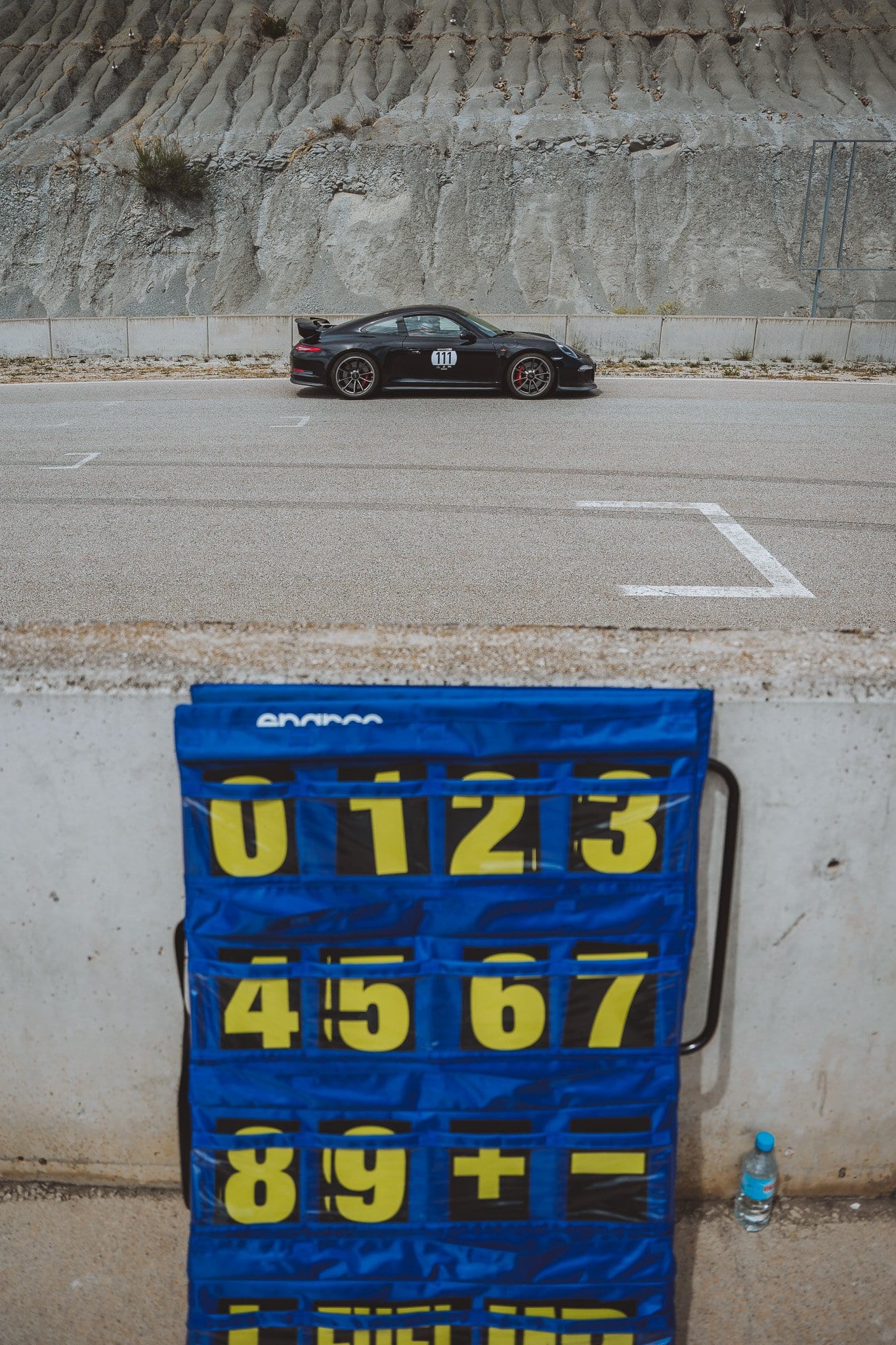 Un 911 negro en pista mientras el panel de señales espera en el muro