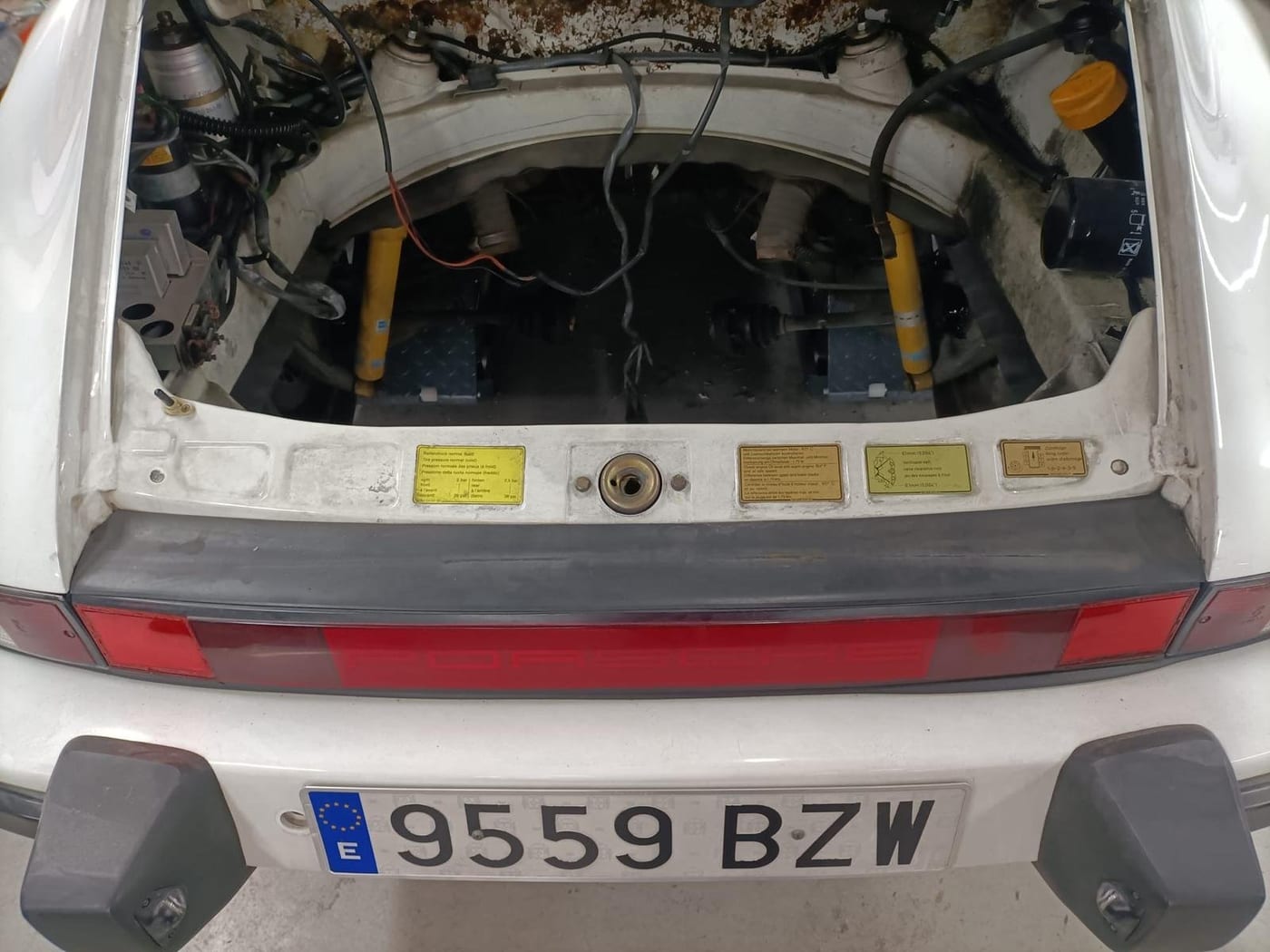 Engine bay of the white G-series 911 with the yellow dampers visible