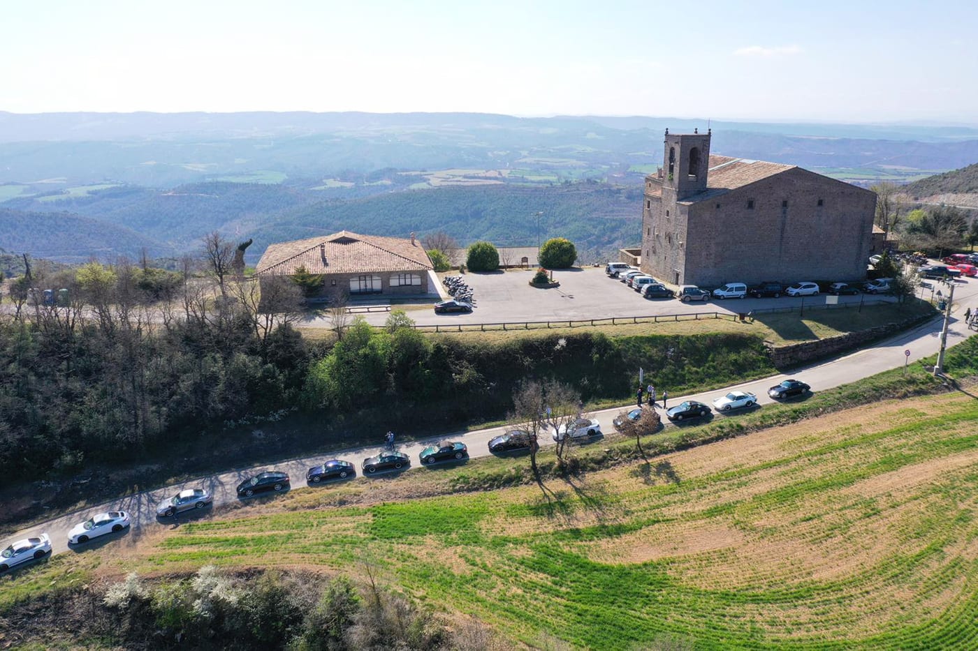 Vista aèria dels Porsche del V Endurance alineats a la carretera al costat d'una església romànica