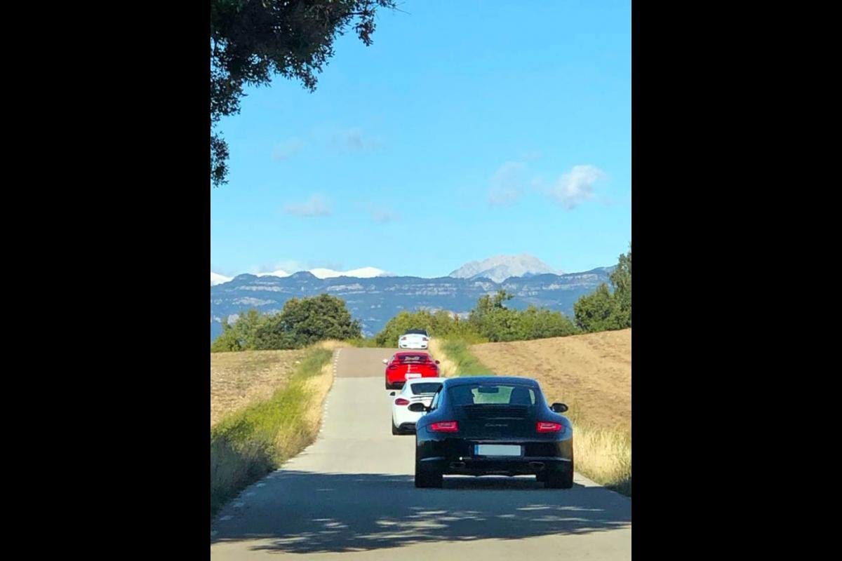 Filera de Porsche per un camí entre camps amb la serra al fons, al 9/11 Rebel Ride