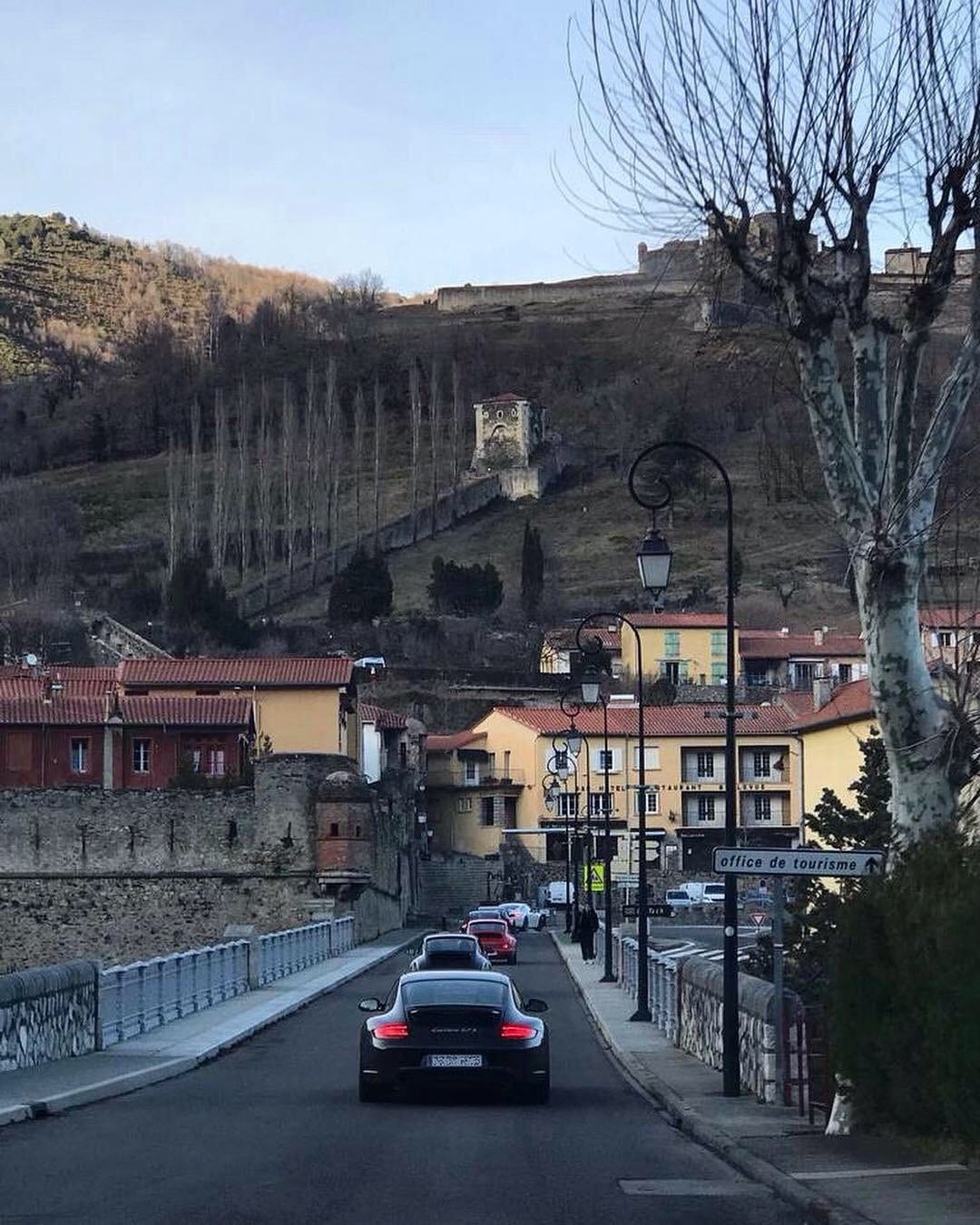 La filera del IV Endurance travessa un poble francès al capvespre, amb la fortalesa sobre el vessant