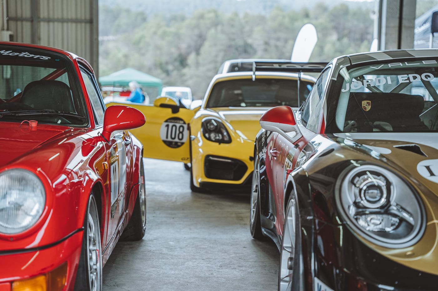 Los coches del equipo alineados a la entrada del box: el 964 rojo, un Cayman amarillo y el 991 dorado
