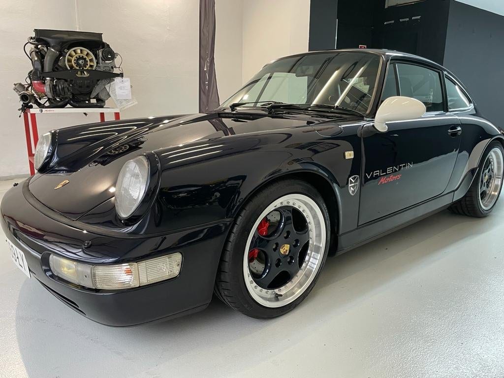 Porsche 964 azul noche con vinilo de Valentín Motors y un motor bóxer en el caballete al fondo