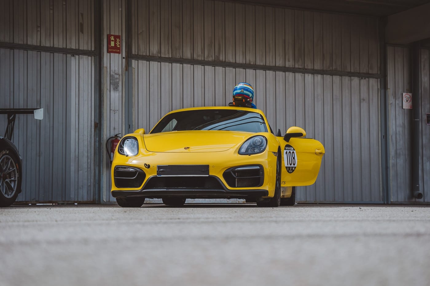 El Cayman GT4 amarillo número 108 con la puerta abierta, ante el box