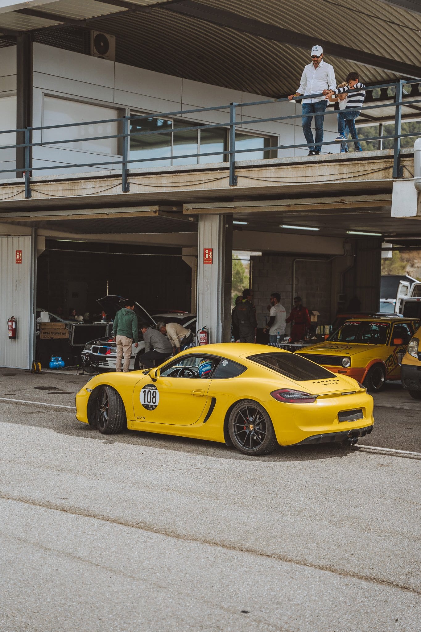 El Cayman GT4 amarillo número 108 saliendo del box hacia la pista