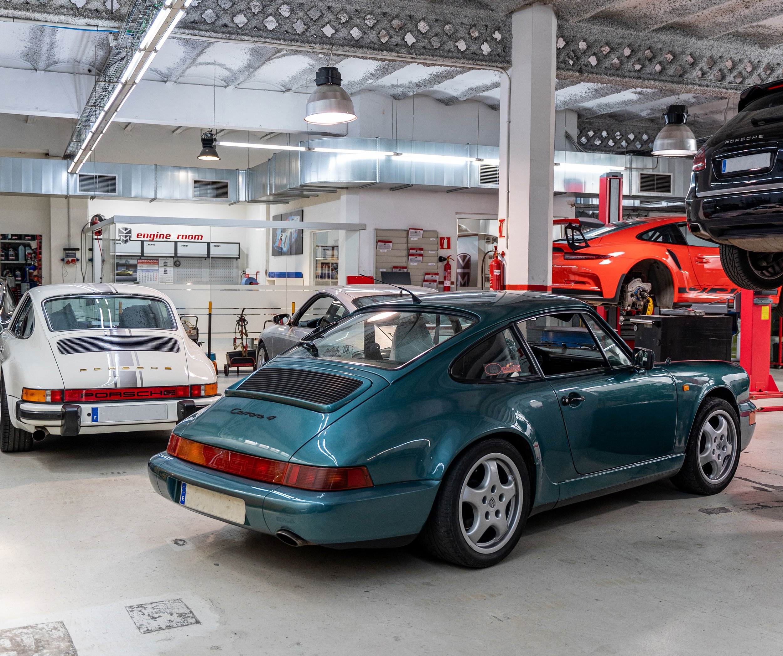 Nave del taller con un 911 964 turquesa y un 911 clásico blanco en primer plano