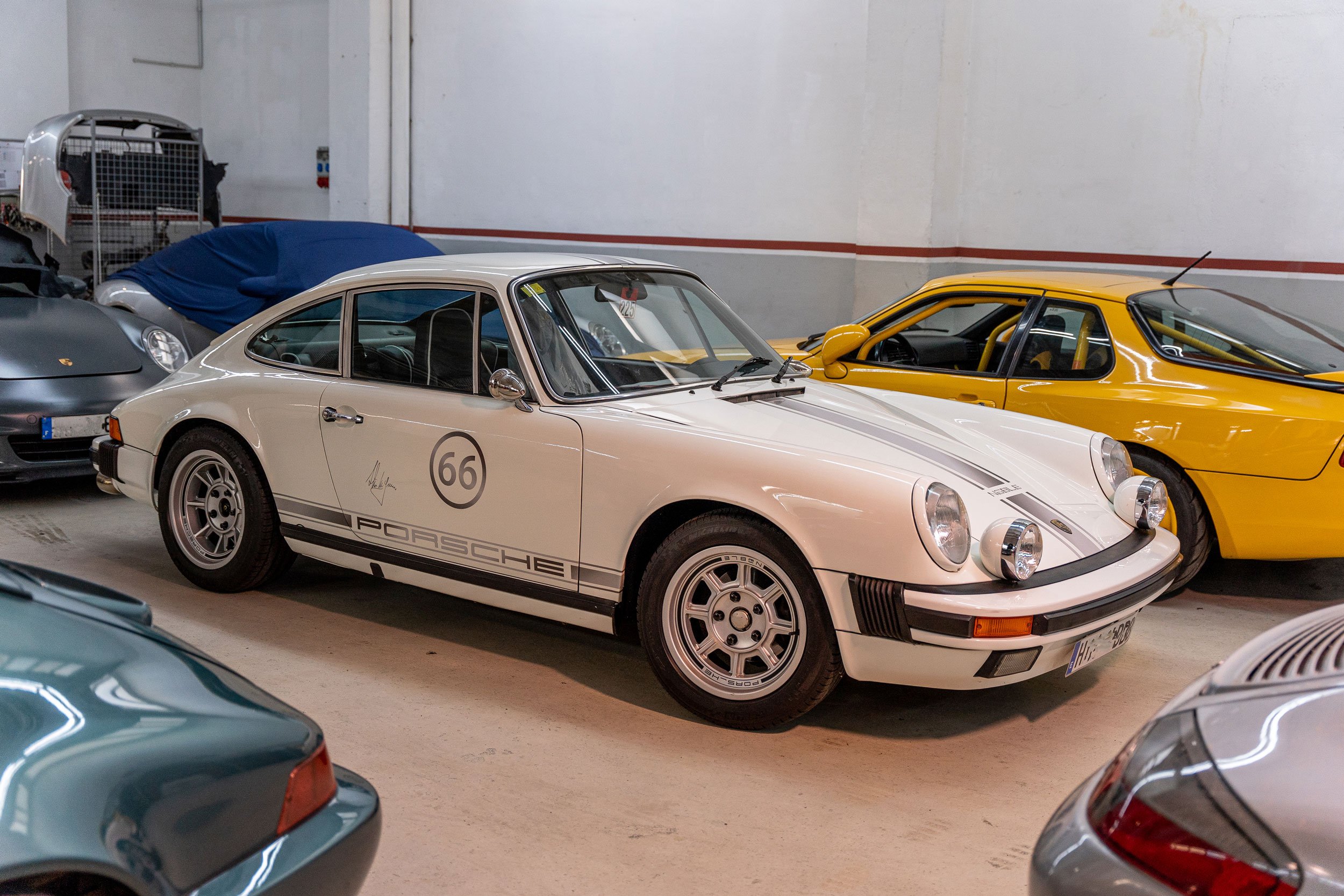 Porsche 911 backdating blanc amb el dorsal 66 a les portes, aparcat entre altres Porsche al taller