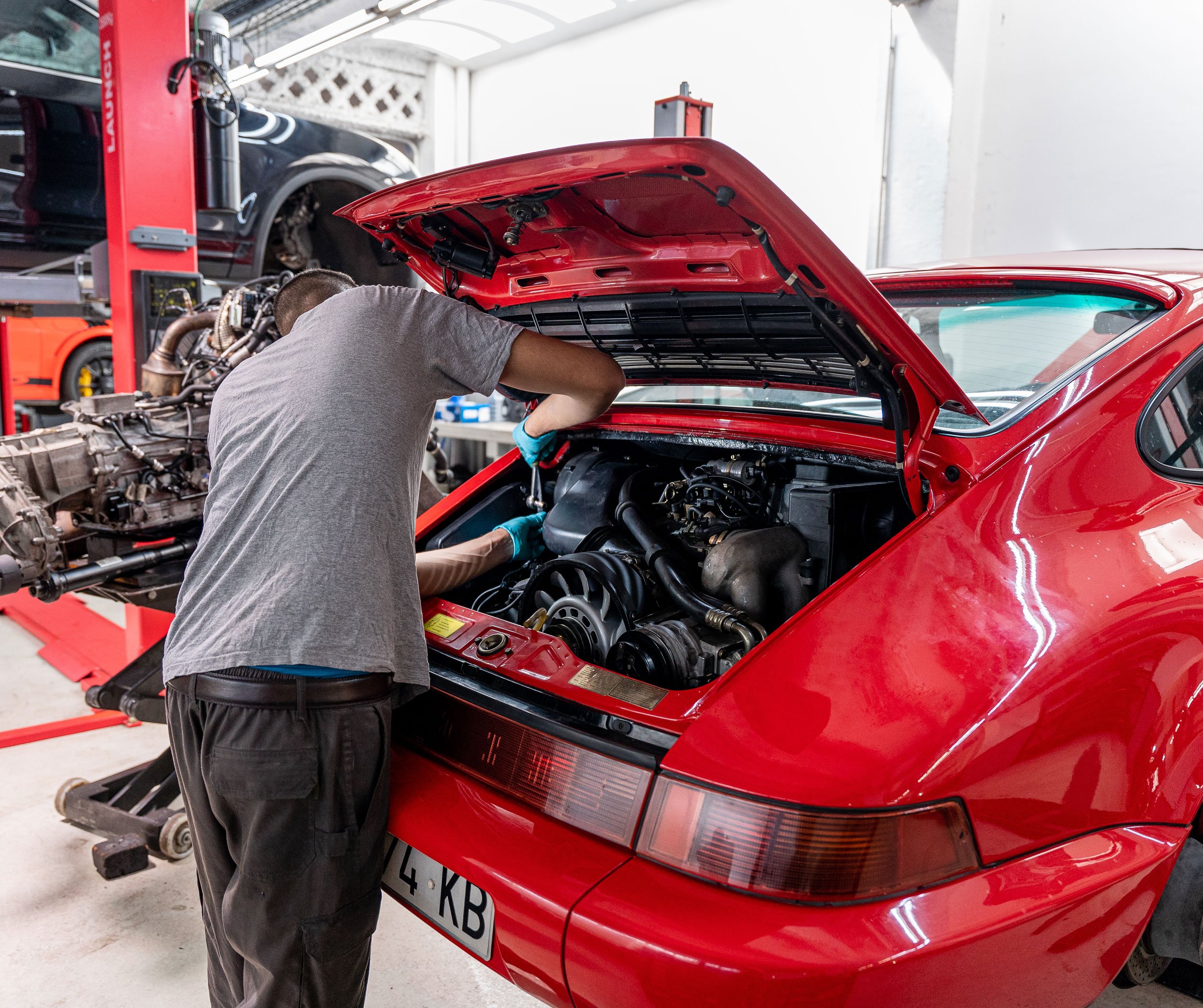 Mecánico inclinado sobre el vano motor de un 964 rojo con la tapa abierta