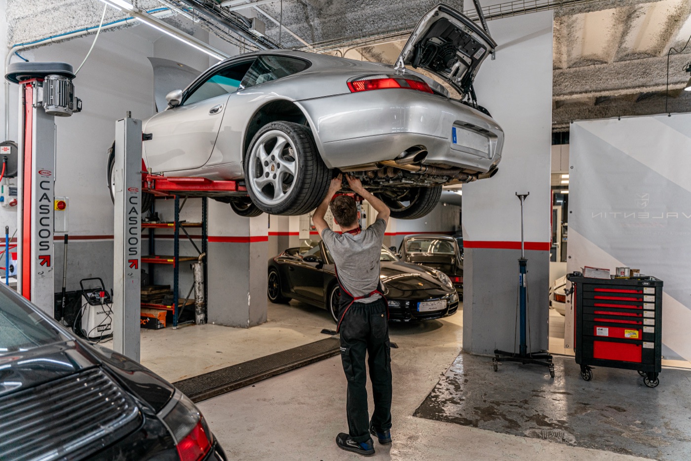 Mecánico revisando los bajos de un Porsche 996 plateado en el elevador