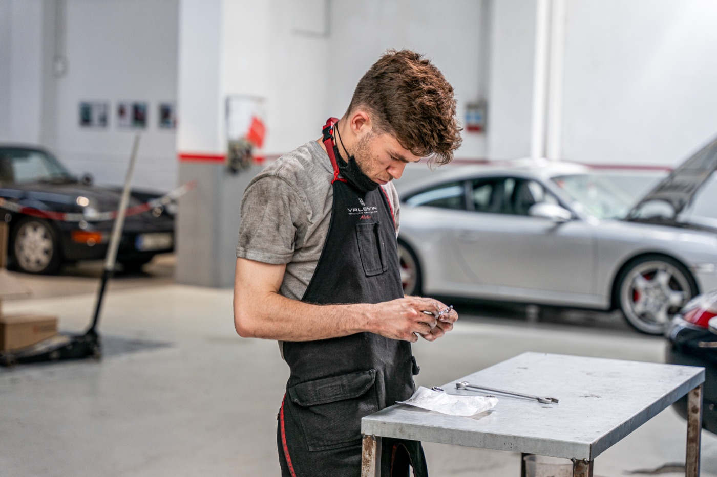Mecánico examinando una pieza junto a un Porsche 911 en el taller