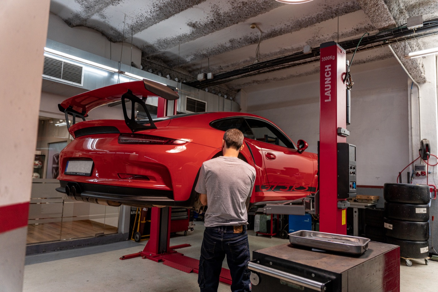 Mecánico revisando un Porsche 911 GT3 RS rojo sobre el elevador del taller