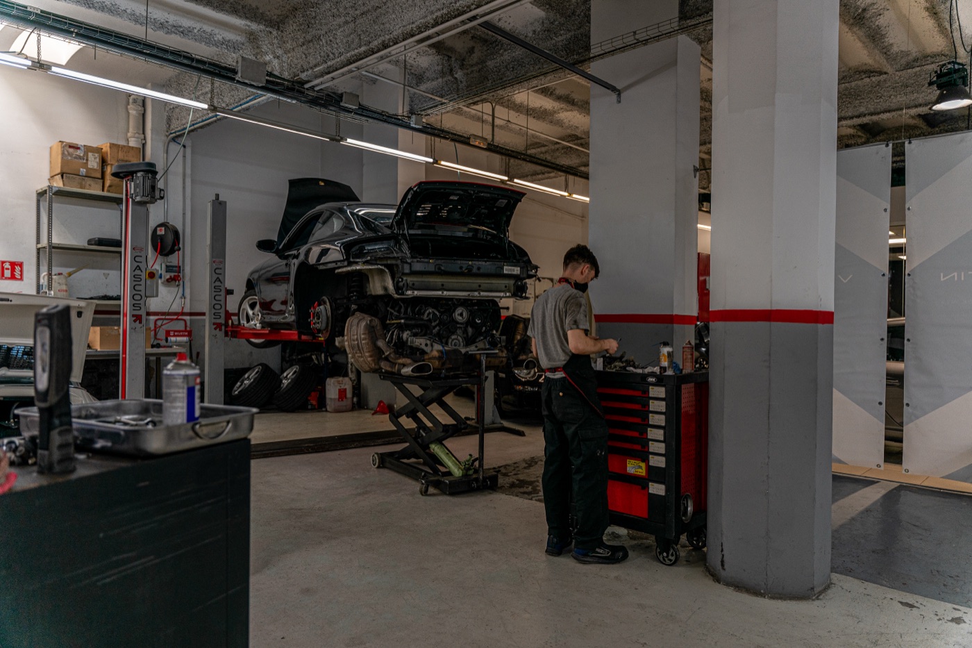 Nave del taller con un Porsche 911 negro en el elevador y un mecánico trabajando